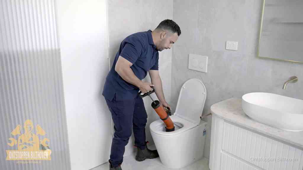 Een monteur buigt over een wandcloset en duwt met de hand een persluchtontstopper in de toiletpot om de verstopping handmatig los te maken in Bilthoven
