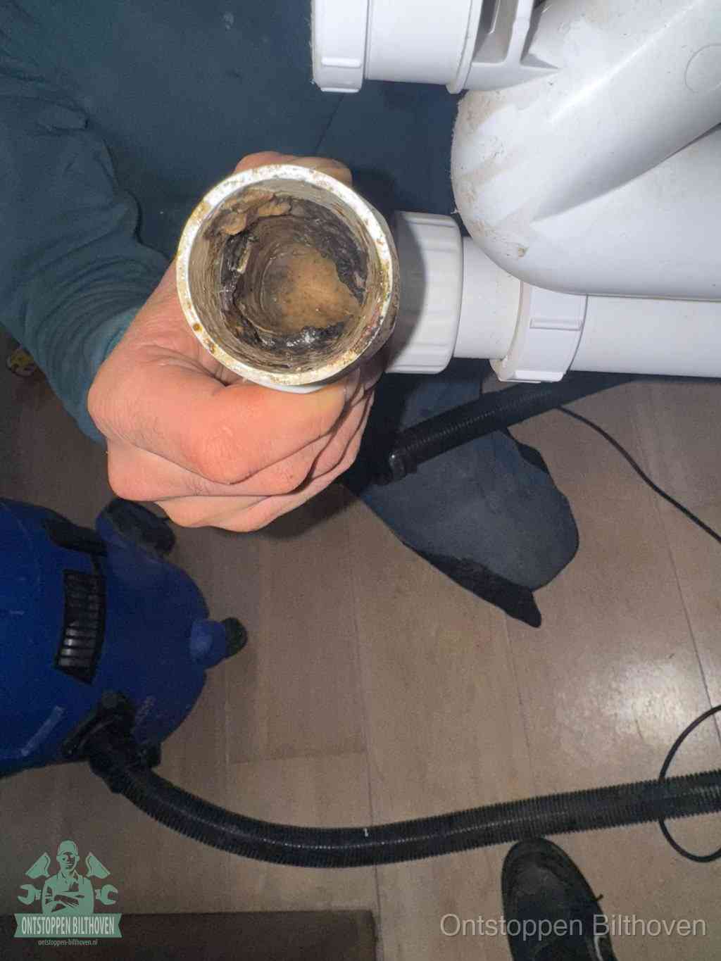 Een hand houdt een losgekoppeld PVC-afvoerbuisstuk vast dat van binnen volledig is dichtgeslibd met vet, vuil en aanslag, de meest voorkomende oorzaak van een verstopte afvoer in Bilthoven
