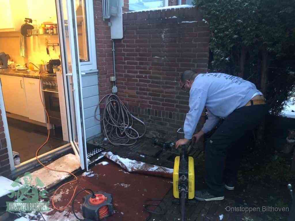 Een monteur werkt buiten bij een open riool-/grondput met een elektrische ontstoppingsmachine om een verborgen afvoerprobleem op te sporen in Bilthoven