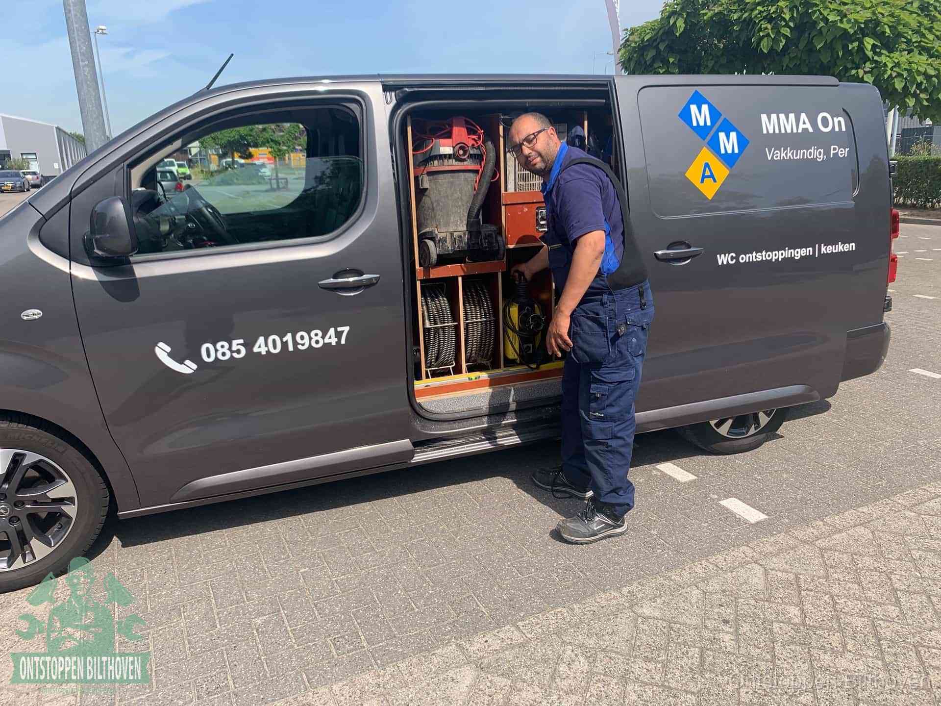 Een monteur bij de open schuifdeur van zijn bedrijfsbus op een parkeerplaats, klaar om de oorzaak van terugkerende afvoerverstoppingen aan te pakken in Bilthoven