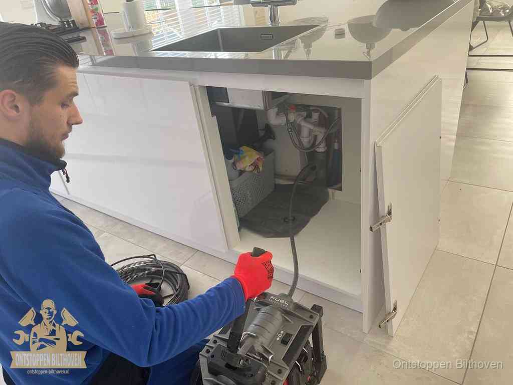 Monteur ontstopt met een veermachine een verstopte afvoer onder de gootsteen in Bilthoven