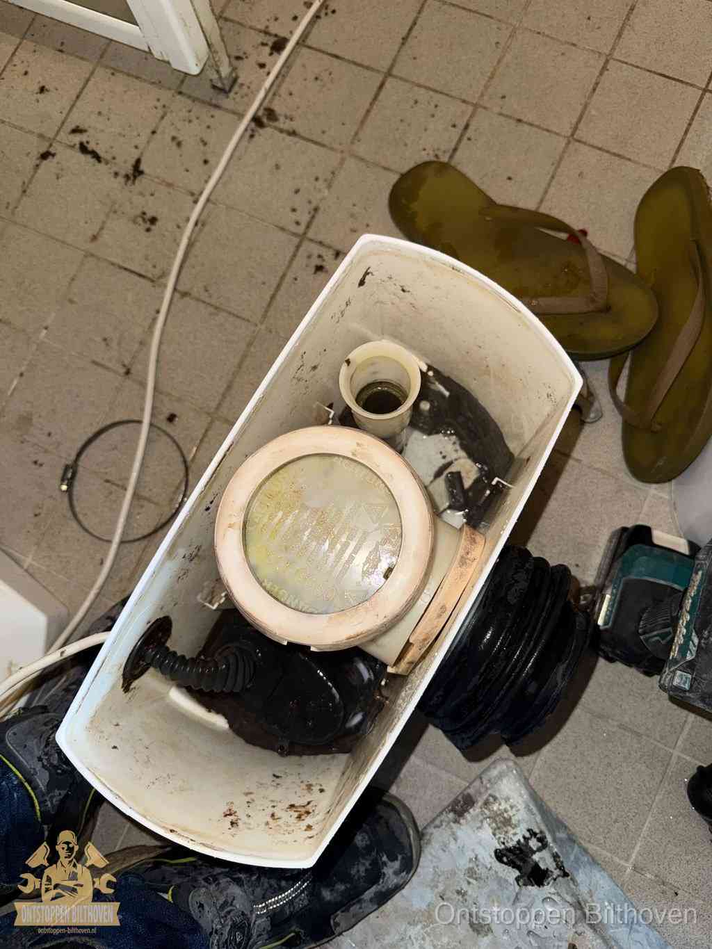 Een gedemonteerde toiletpot op de vloer met ontstoppingsveer en gereedschap ernaast, het verwijderen van een vastzittend voorwerp uit de wc in Bilthoven