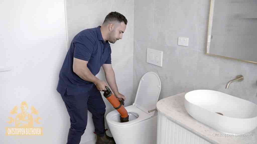Een man gebruikt een handmatige luchtdruk-ontstopper in een modern betegeld toilet om zelf de wc te ontstoppen in Bilthoven